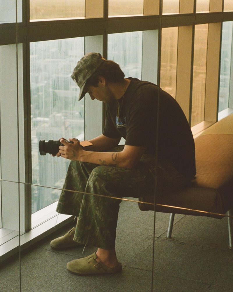 Azariah checking his camera by a high-rise window over a city